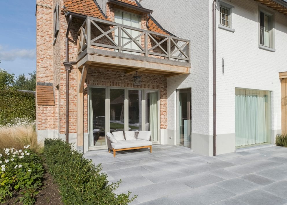 Geschuurde blauwe steen in banenpatroon rond landelijke woning met wit gevelpleister en rode baksteen